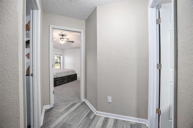 corridor with a textured ceiling and light hardwood / wood-style flooring