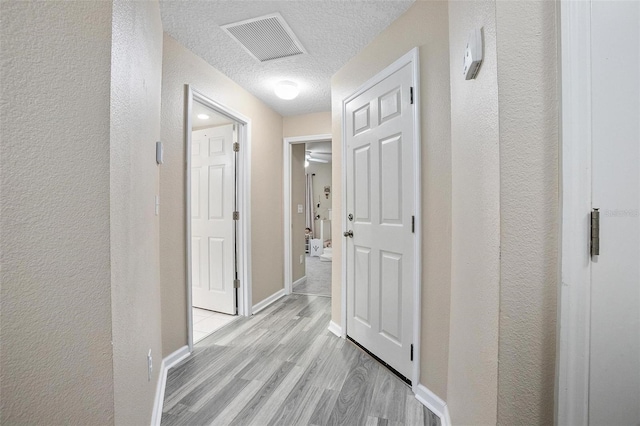 hallway with light hardwood / wood-style flooring and a textured ceiling