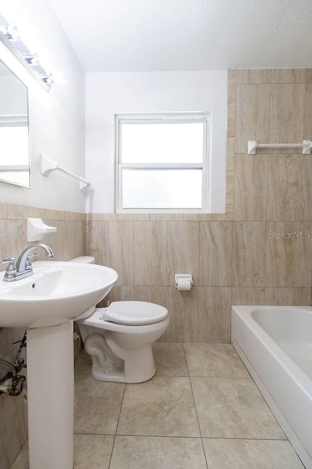 bathroom featuring a bath, tile patterned floors, a textured ceiling, toilet, and tile walls