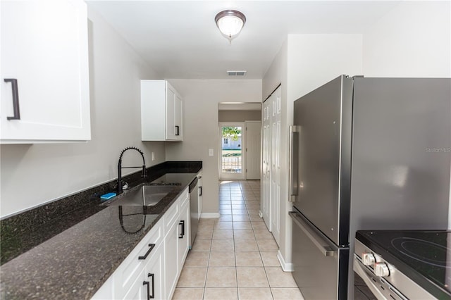 kitchen featuring dark stone counters, white cabinets, sink, light tile patterned floors, and stainless steel appliances