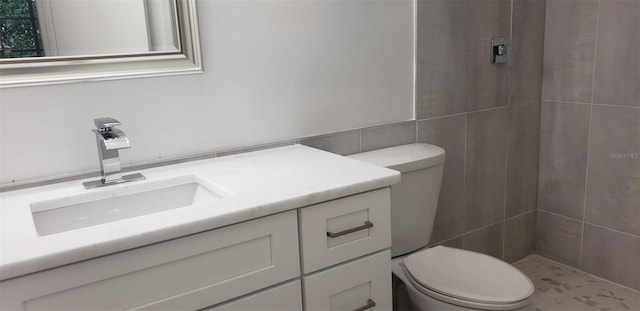 bathroom featuring vanity, toilet, tile walls, and a tile shower