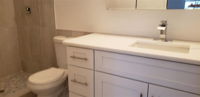 bathroom with a tile shower, vanity, and toilet