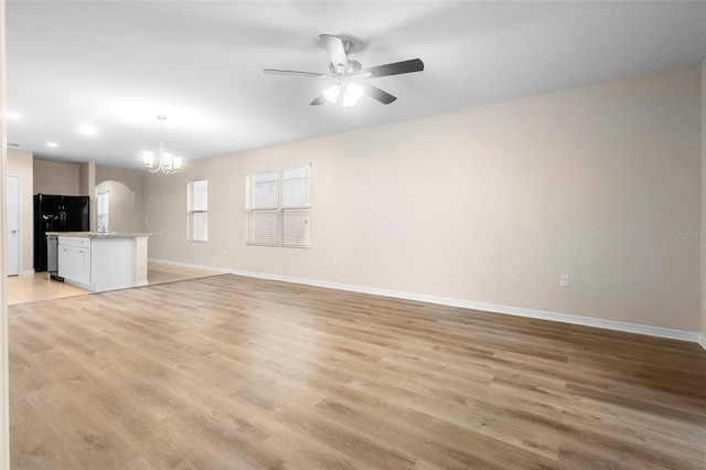 unfurnished living room with ceiling fan with notable chandelier and light hardwood / wood-style floors