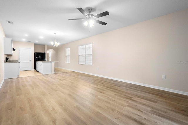 unfurnished living room with ceiling fan with notable chandelier and light hardwood / wood-style flooring