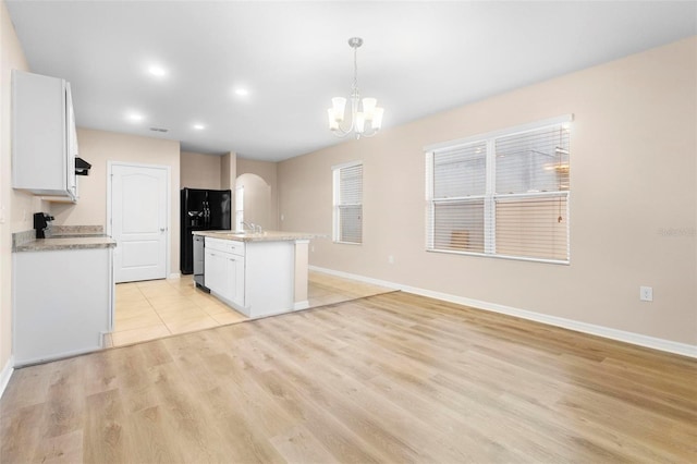 kitchen with white cabinets, hanging light fixtures, black fridge with ice dispenser, a center island with sink, and light wood-type flooring