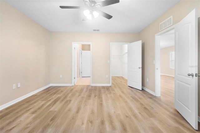 unfurnished bedroom featuring a closet, a spacious closet, ceiling fan, and light hardwood / wood-style flooring