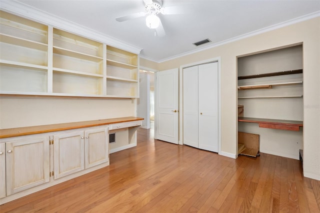 unfurnished office with ornamental molding, built in desk, ceiling fan, and light wood-type flooring