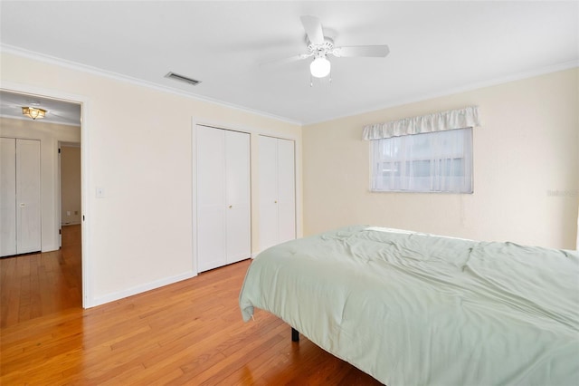 bedroom with two closets, wood-type flooring, and ornamental molding