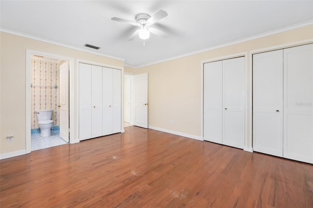 unfurnished bedroom featuring hardwood / wood-style flooring, ornamental molding, and two closets