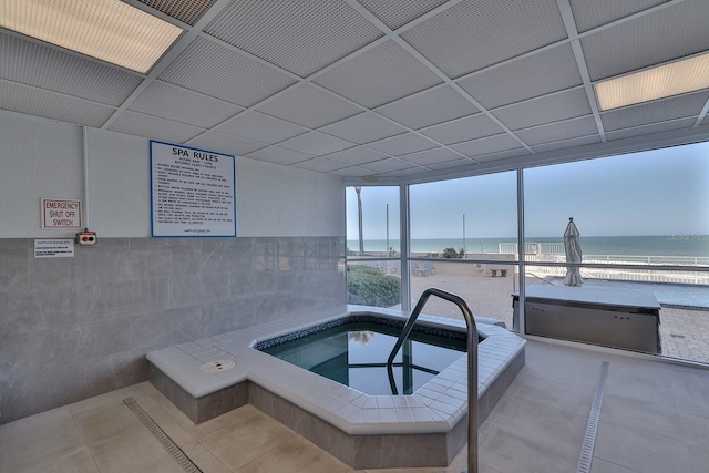 view of swimming pool featuring a beach view, an indoor hot tub, and a water view