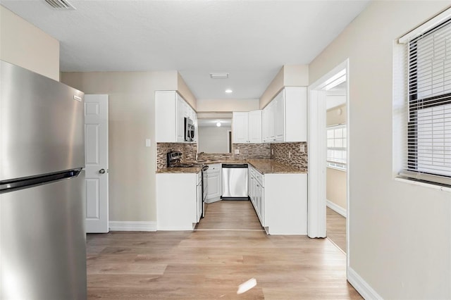 kitchen with backsplash, white cabinetry, stainless steel appliances, and light hardwood / wood-style floors