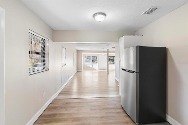 hall featuring light wood-type flooring, a textured ceiling, and a wealth of natural light