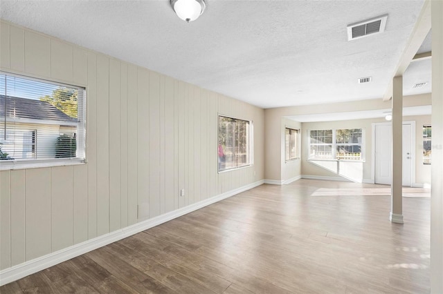 spare room featuring wood walls, a textured ceiling, and light hardwood / wood-style flooring