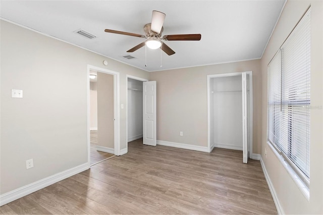 unfurnished bedroom featuring multiple closets, ceiling fan, light hardwood / wood-style flooring, and crown molding