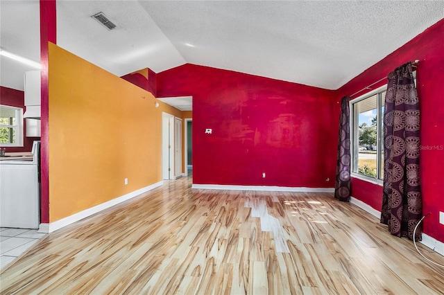 empty room featuring a textured ceiling, light hardwood / wood-style floors, and lofted ceiling