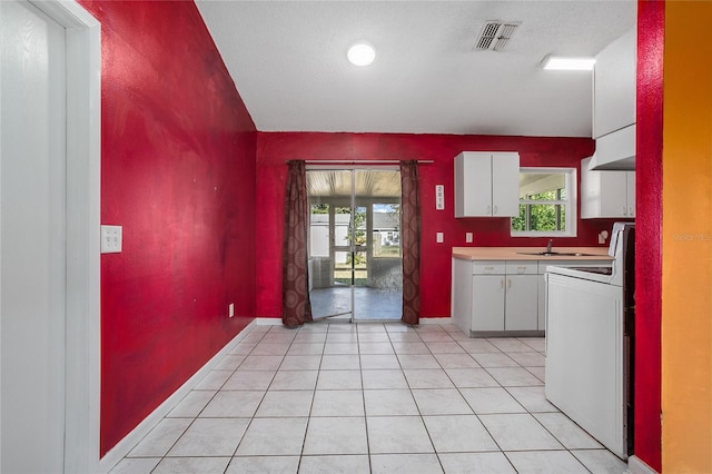 kitchen featuring white range with electric stovetop, white cabinets, a healthy amount of sunlight, and light tile patterned floors