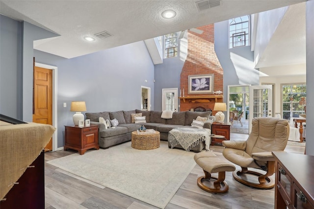 living room featuring high vaulted ceiling, a textured ceiling, and light wood-type flooring