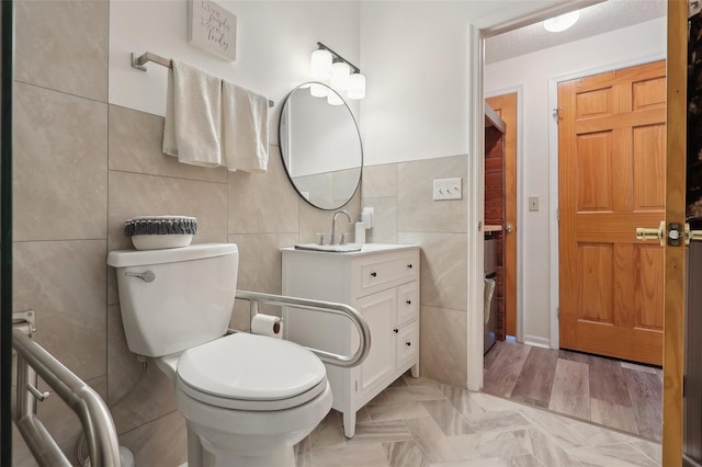 bathroom featuring hardwood / wood-style floors, vanity, toilet, tile walls, and a textured ceiling