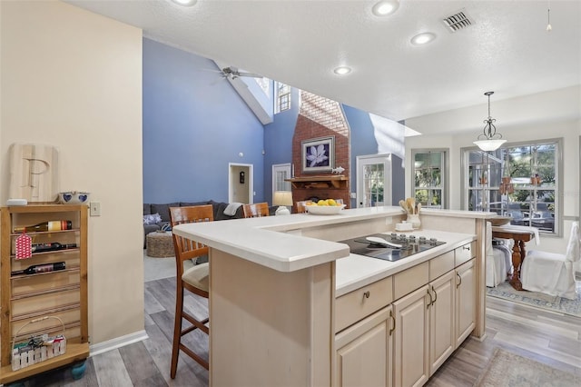 kitchen with a center island, hanging light fixtures, a kitchen breakfast bar, light hardwood / wood-style floors, and black electric stovetop