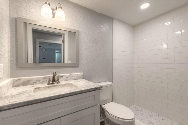 bathroom featuring tiled shower, vanity, and toilet