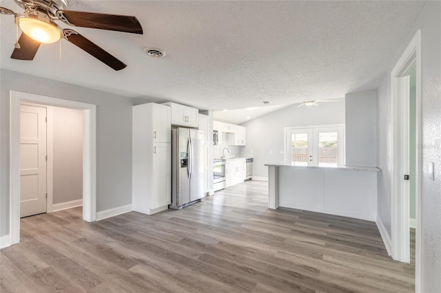 unfurnished living room with vaulted ceiling, french doors, a textured ceiling, and light wood-type flooring