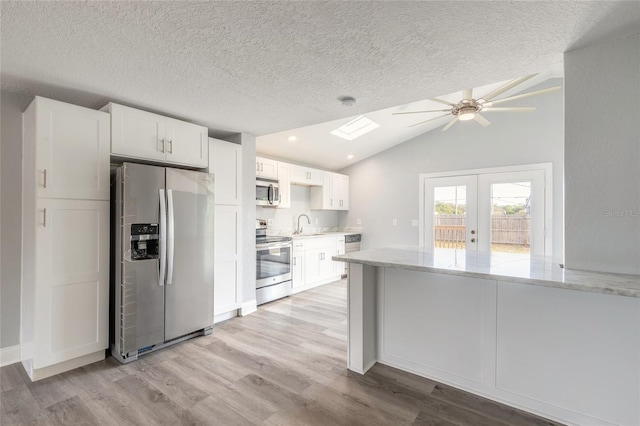 kitchen featuring light stone countertops, vaulted ceiling with skylight, white cabinets, and appliances with stainless steel finishes