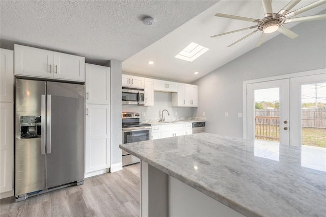 kitchen with appliances with stainless steel finishes, vaulted ceiling with skylight, white cabinetry, and sink