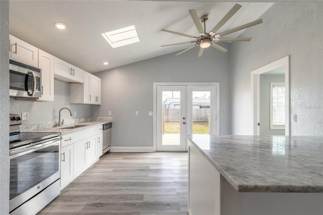 kitchen with sink, appliances with stainless steel finishes, lofted ceiling with skylight, white cabinets, and light wood-type flooring