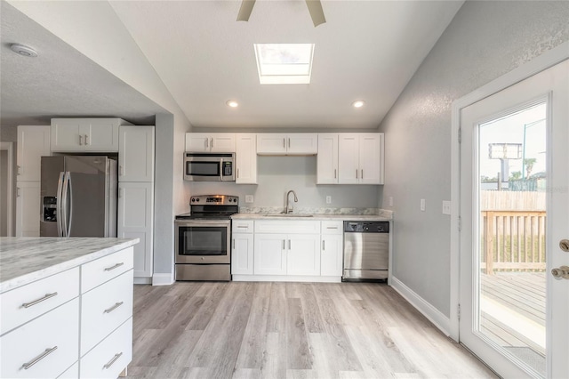 kitchen with vaulted ceiling with skylight, stainless steel appliances, white cabinetry, and sink