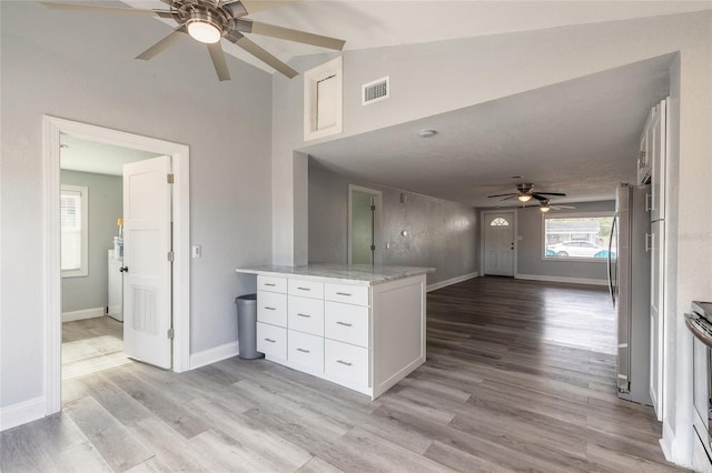 kitchen with lofted ceiling, light hardwood / wood-style flooring, light stone countertops, white cabinetry, and stainless steel appliances