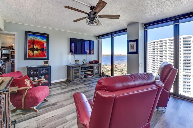 living room with ceiling fan, wood-type flooring, a textured ceiling, and a wall of windows