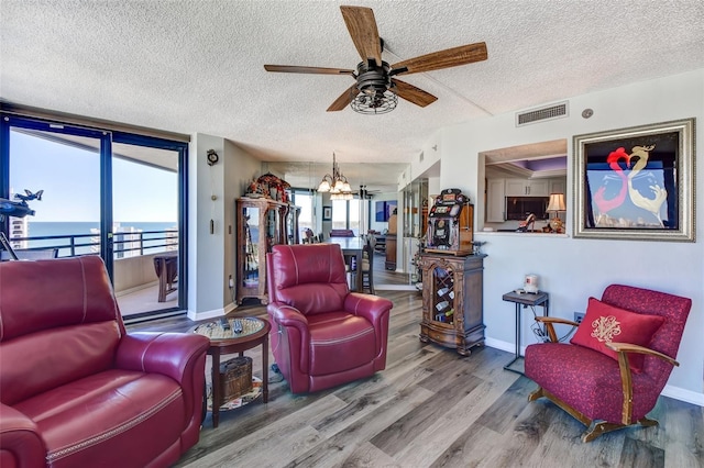 living room with ceiling fan with notable chandelier, wood-type flooring, a textured ceiling, and a water view