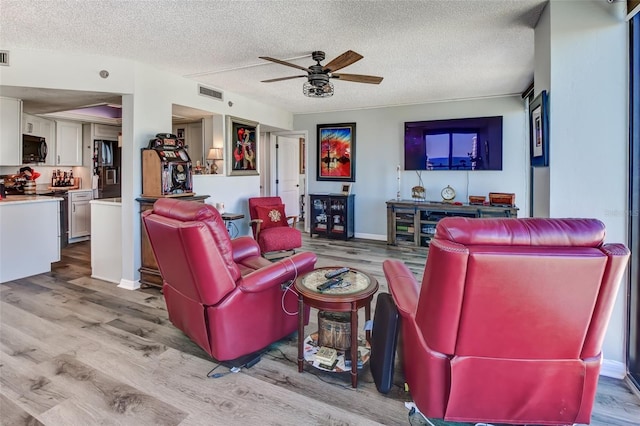 living room with ceiling fan, light hardwood / wood-style floors, and a textured ceiling