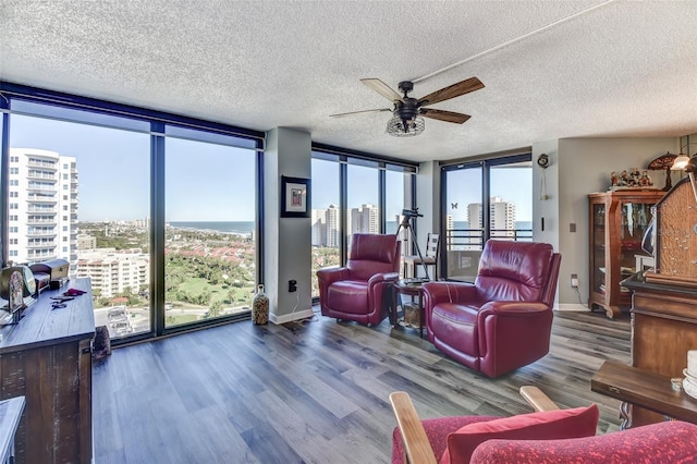 living room with ceiling fan, wood-type flooring, a textured ceiling, and a wall of windows