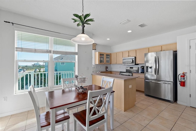 kitchen featuring light brown cabinets, hanging light fixtures, a textured ceiling, a kitchen island, and appliances with stainless steel finishes