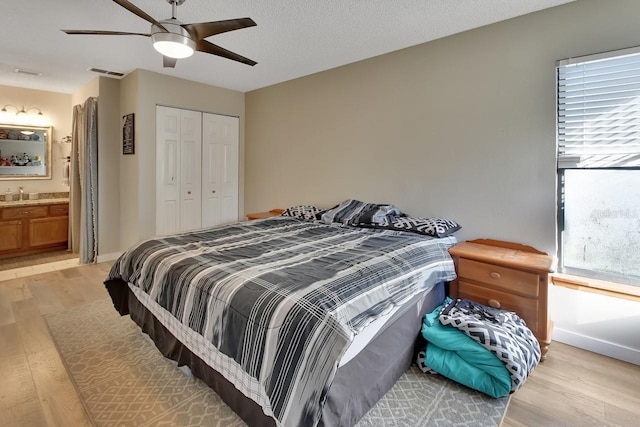 bedroom featuring connected bathroom, ceiling fan, light hardwood / wood-style flooring, a textured ceiling, and a closet