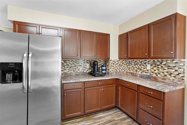 kitchen featuring light stone counters, stainless steel fridge with ice dispenser, light hardwood / wood-style flooring, and tasteful backsplash