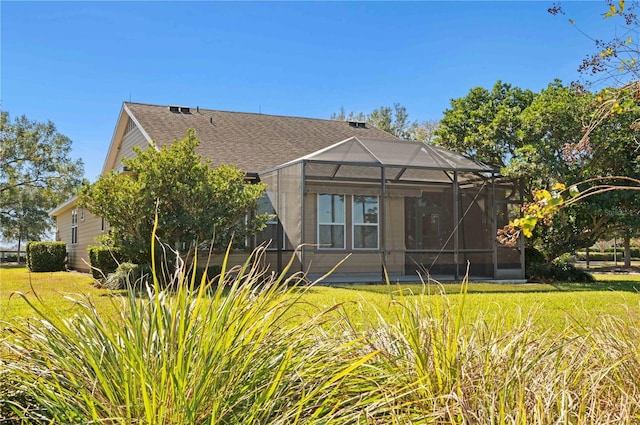 rear view of house with glass enclosure and a lawn