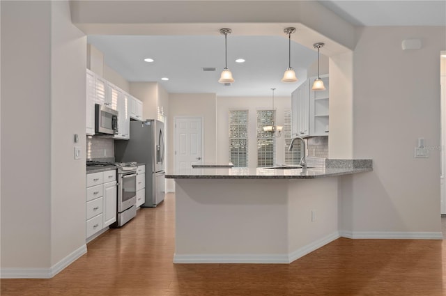 kitchen with white cabinets, appliances with stainless steel finishes, kitchen peninsula, and wood-type flooring