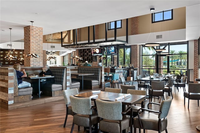 dining area with hardwood / wood-style floors, a towering ceiling, and brick wall