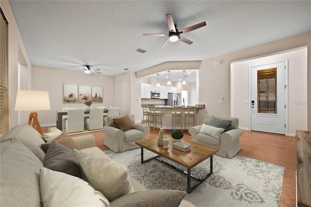 living room with a textured ceiling, light hardwood / wood-style floors, and ceiling fan