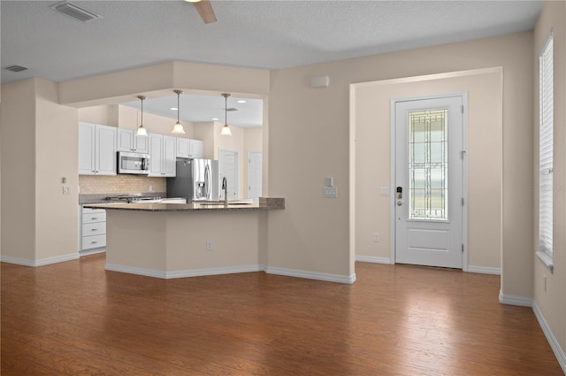 kitchen featuring hardwood / wood-style flooring, decorative light fixtures, white cabinetry, kitchen peninsula, and stainless steel appliances