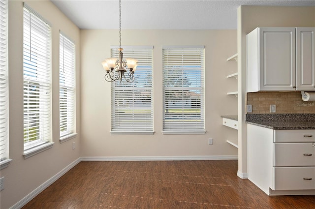 unfurnished dining area featuring a chandelier, a textured ceiling, plenty of natural light, and dark wood-type flooring