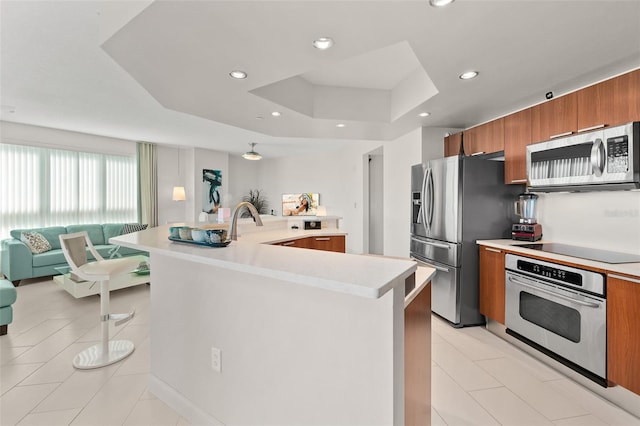 kitchen featuring a kitchen breakfast bar, an island with sink, a tray ceiling, light tile patterned floors, and appliances with stainless steel finishes