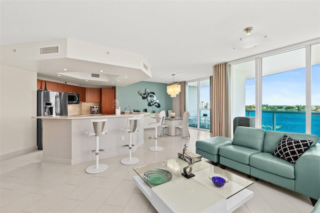 tiled living room featuring expansive windows, a water view, and an inviting chandelier