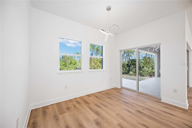 unfurnished room with plenty of natural light, light hardwood / wood-style floors, and a chandelier