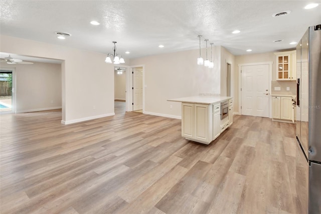 kitchen with pendant lighting, a center island, cream cabinets, light hardwood / wood-style floors, and stainless steel appliances