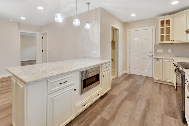 kitchen featuring backsplash, light stone countertops, appliances with stainless steel finishes, decorative light fixtures, and light hardwood / wood-style floors