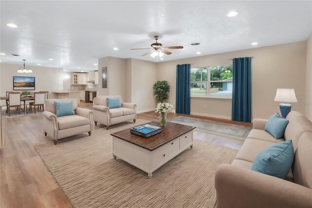 living room with ceiling fan with notable chandelier and light hardwood / wood-style floors