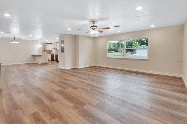 unfurnished living room with a textured ceiling, ceiling fan with notable chandelier, and light wood-type flooring